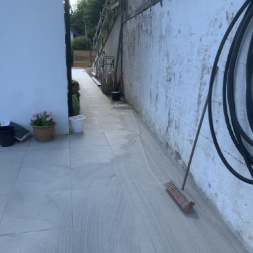 Belægning langs husmur under udførelse med fokus på fald og afvanding