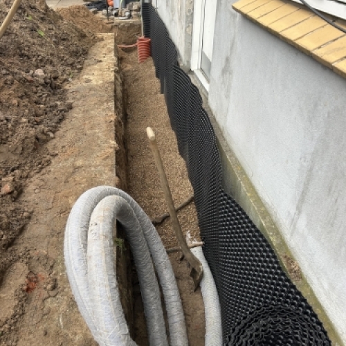 Kloakmester udfører kloakarbejde og drænløsning langs husmur for bedre afvanding
