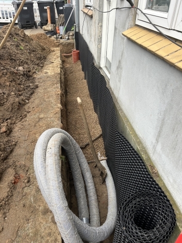 Kloakmester udfører kloakarbejde og drænløsning langs husmur for bedre afvanding